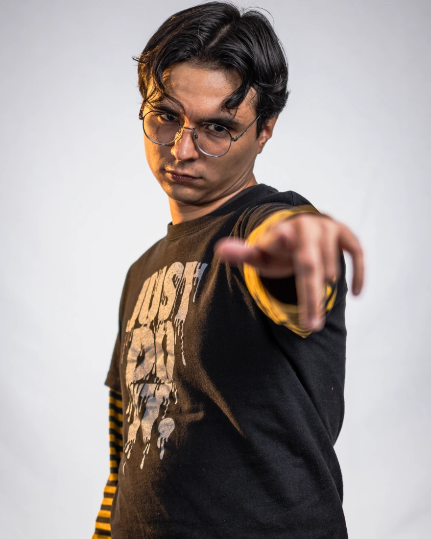 Ahrimix con lentes y una camiseta sobre mangas a rayas amarillas, señalando a la cámara